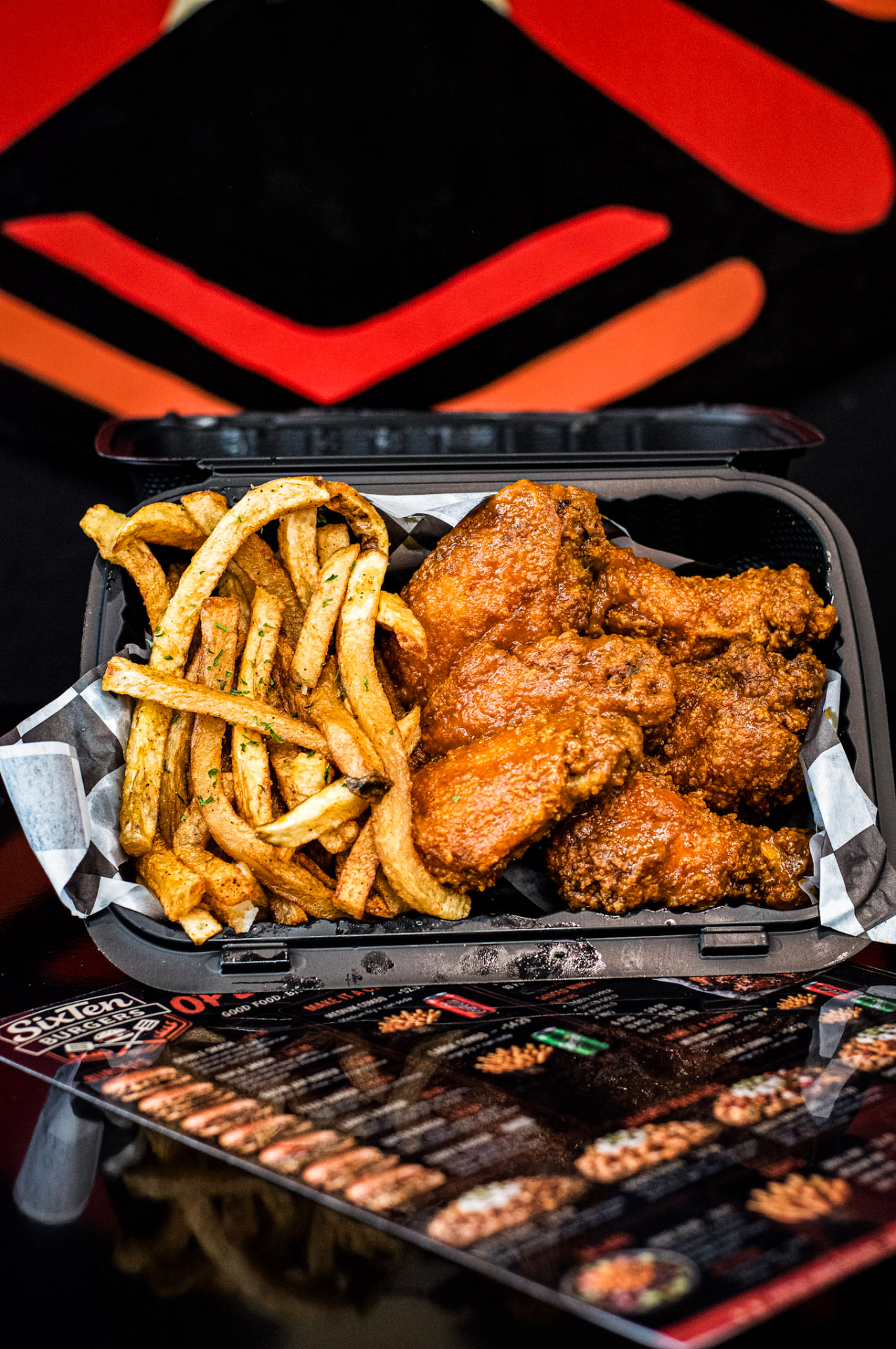 Saucy buffalo wings with seasoned fries in a SixTen takeout box